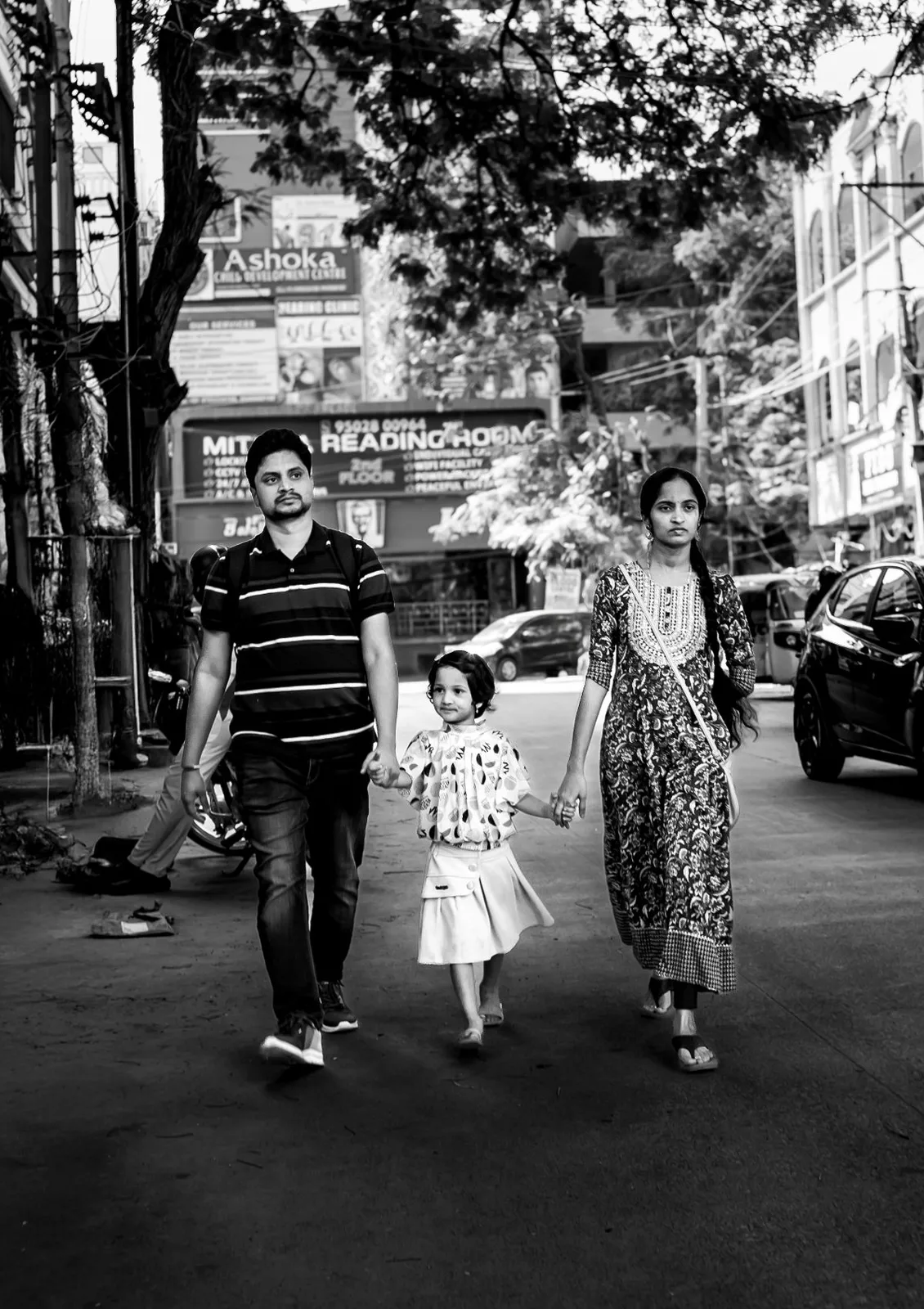 A family walks together on a city street in a candid black and white photo.