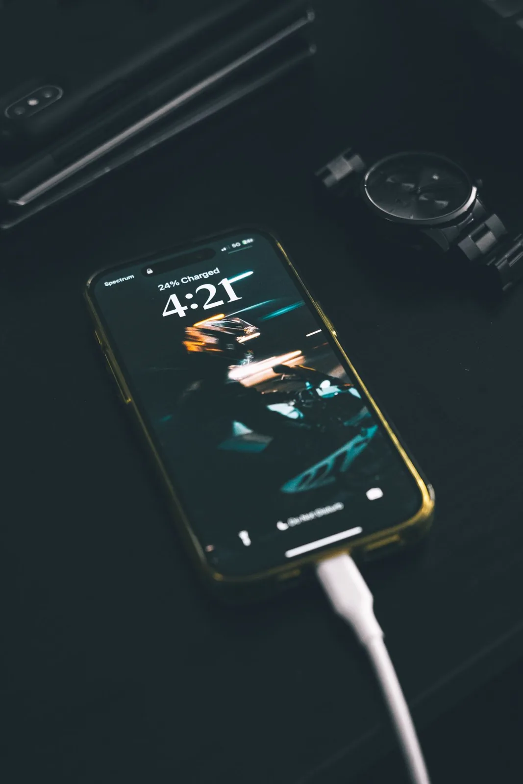 Smartphone charging on a dark wooden table with a digital watch nearby.