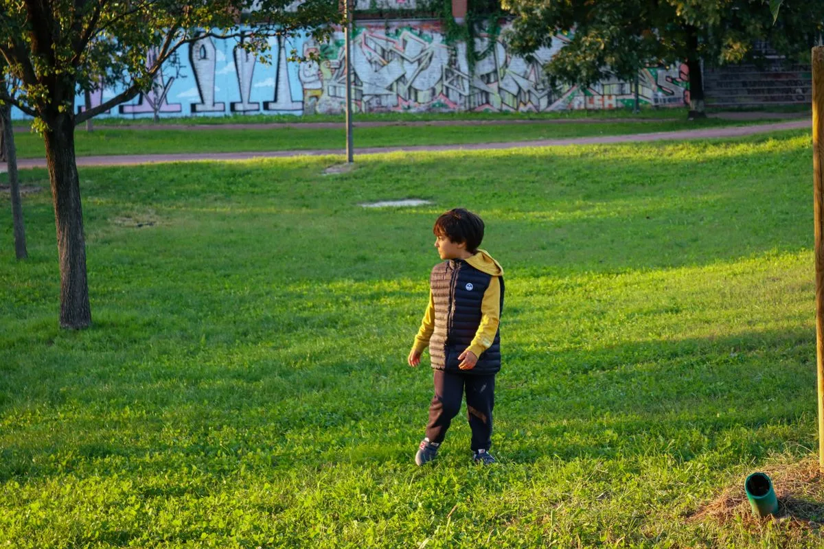 A child in a colorful jacket enjoys a sunny day in a graffiti-styled urban park.