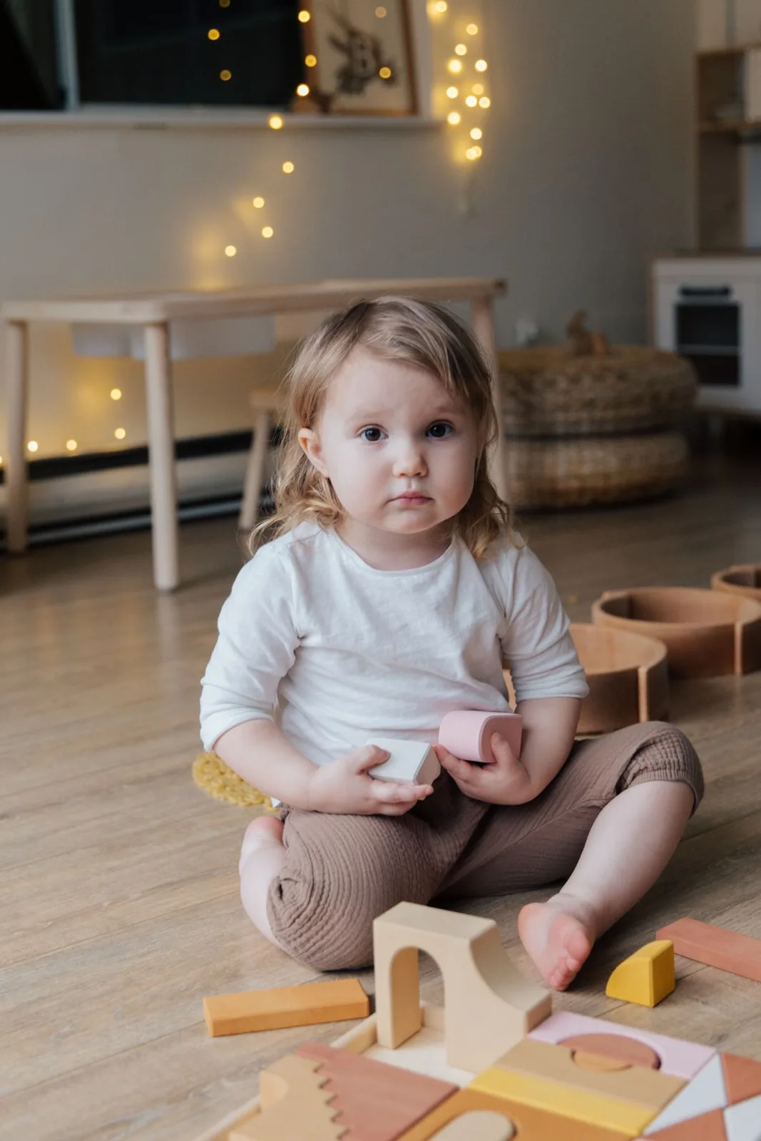 Cute toddler playing with wooden blocks on the floor indoors, surrounded by warm lighting.