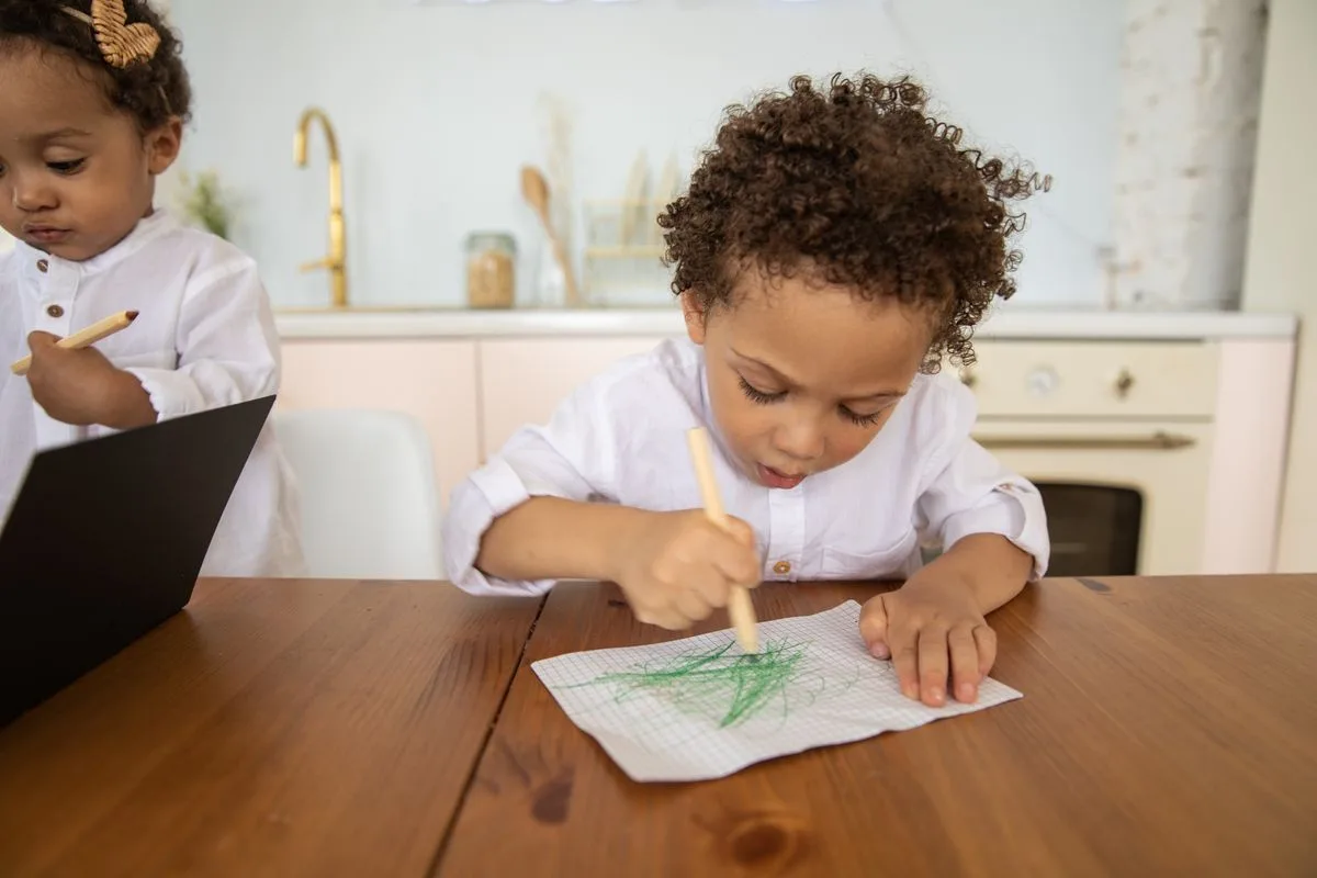 Two young children enjoy drawing indoors at a kitchen table.