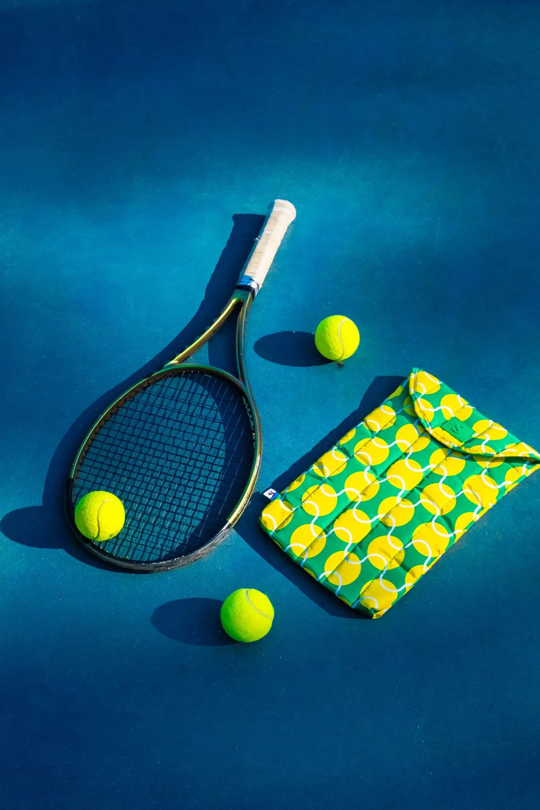 Flat lay of tennis gear showcasing a racket, balls, and sports bag on a blue court.