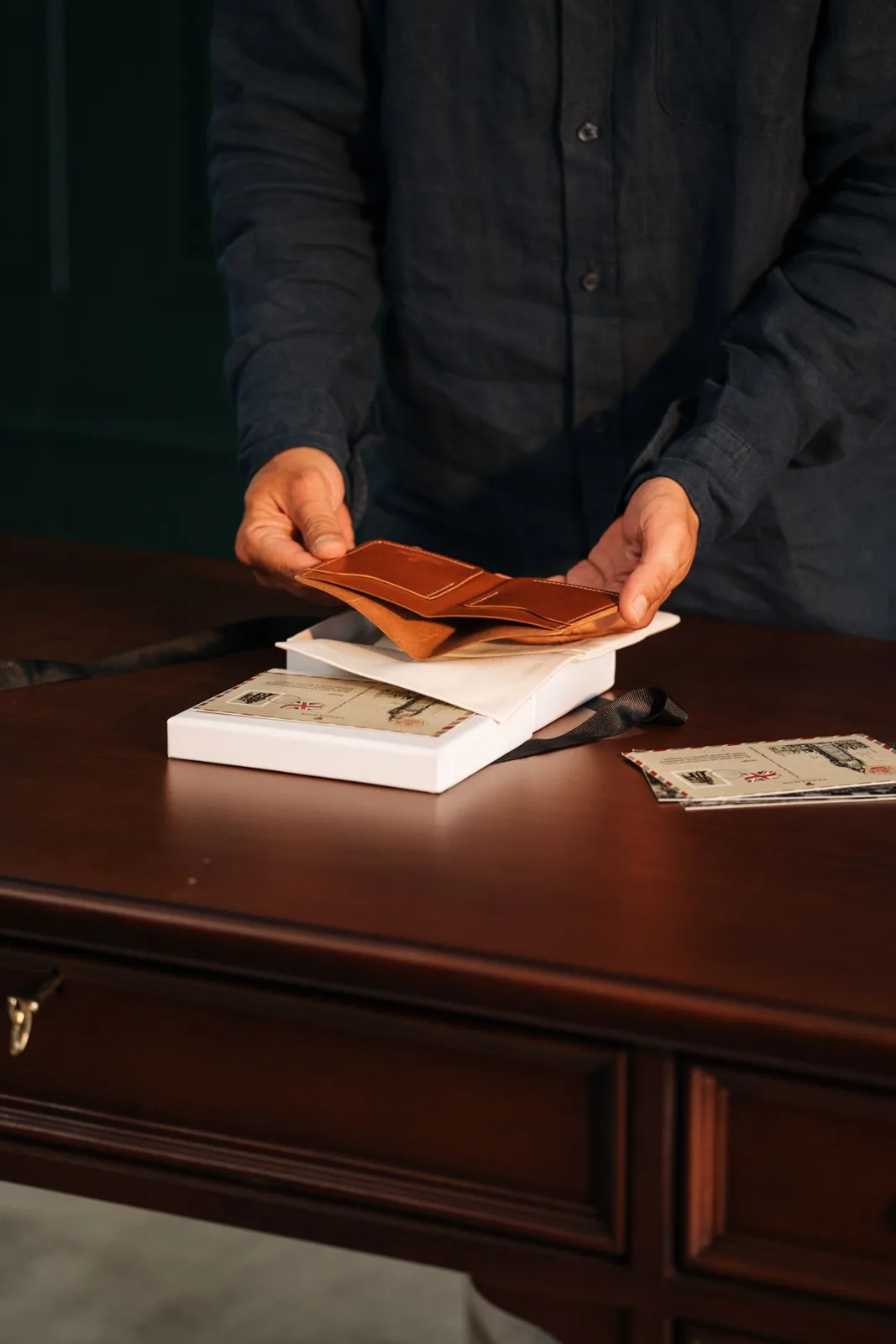 A person organizing envelopes and a leather wallet on a wooden desk.