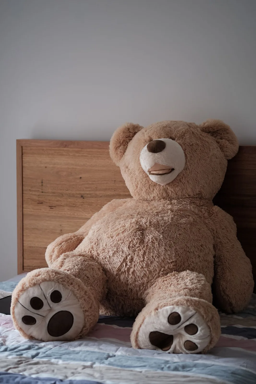 A large plush teddy bear sitting on a neatly made bed in a cozy indoor setting.