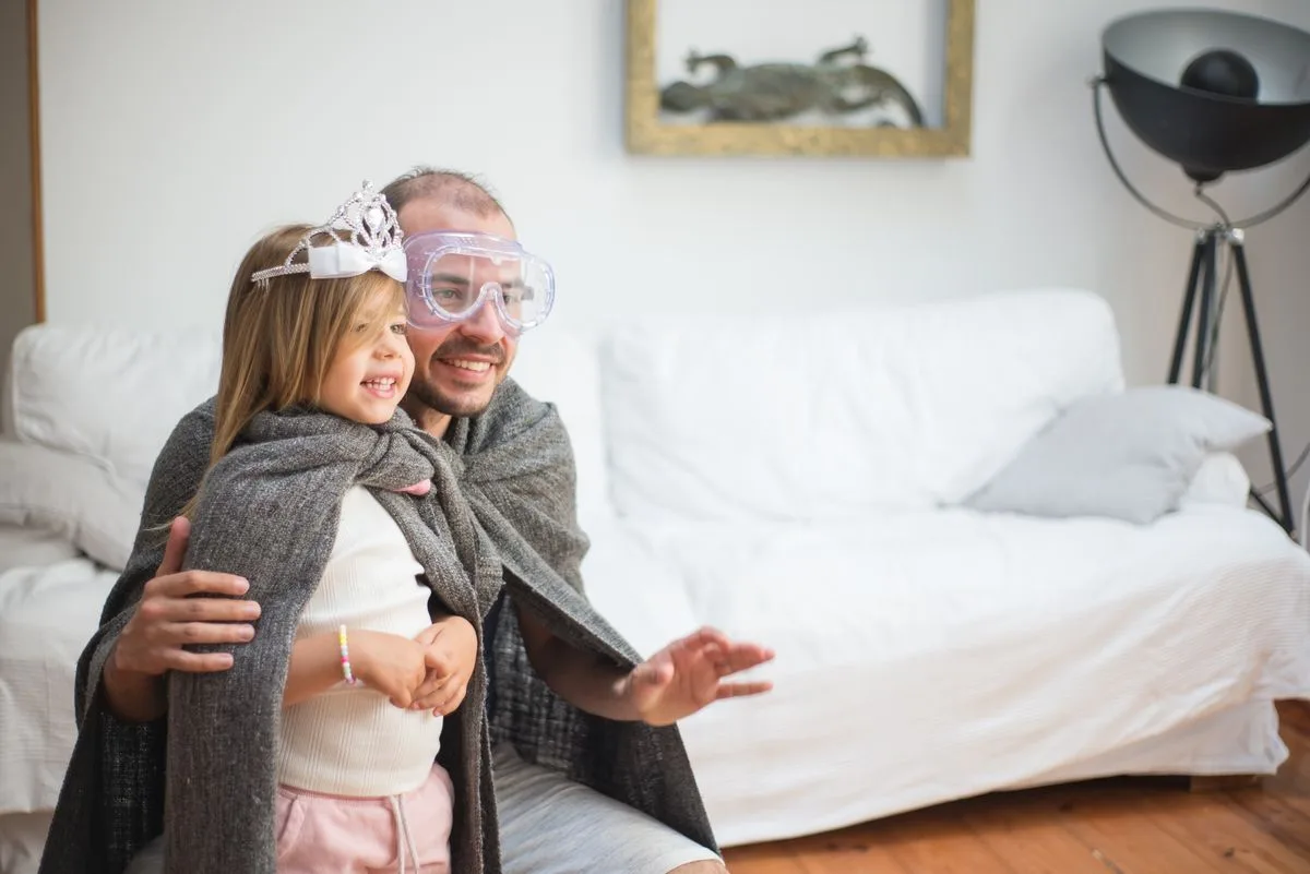 Playful father and daughter dressed in capes, enjoying a fun bonding moment at home.