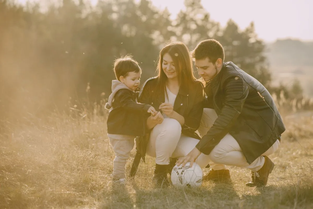 A cheerful family bonding outdoors with a soccer ball, enjoying a sunny day in the grass.