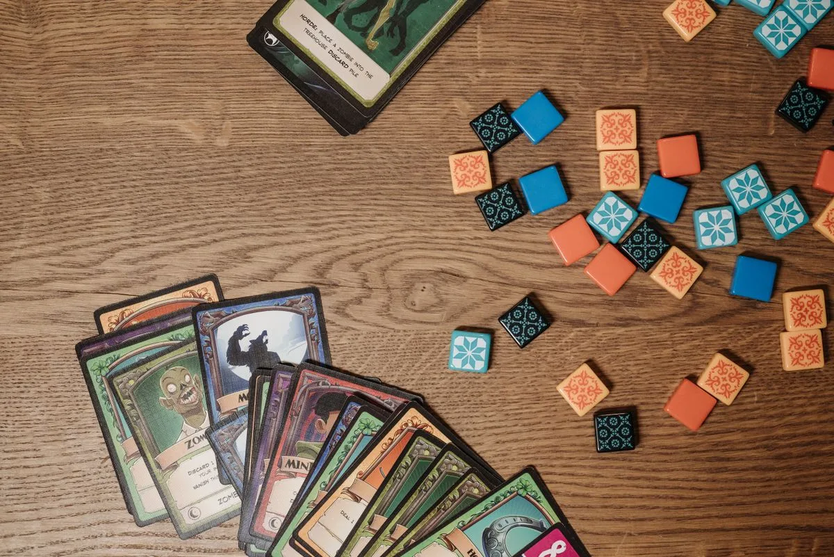 Top view of colorful board game cards and tokens on a wooden table.
