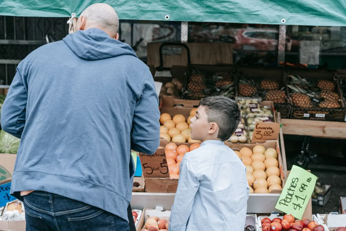 Father and son explore a bustling farmer's market filled with fresh produce.